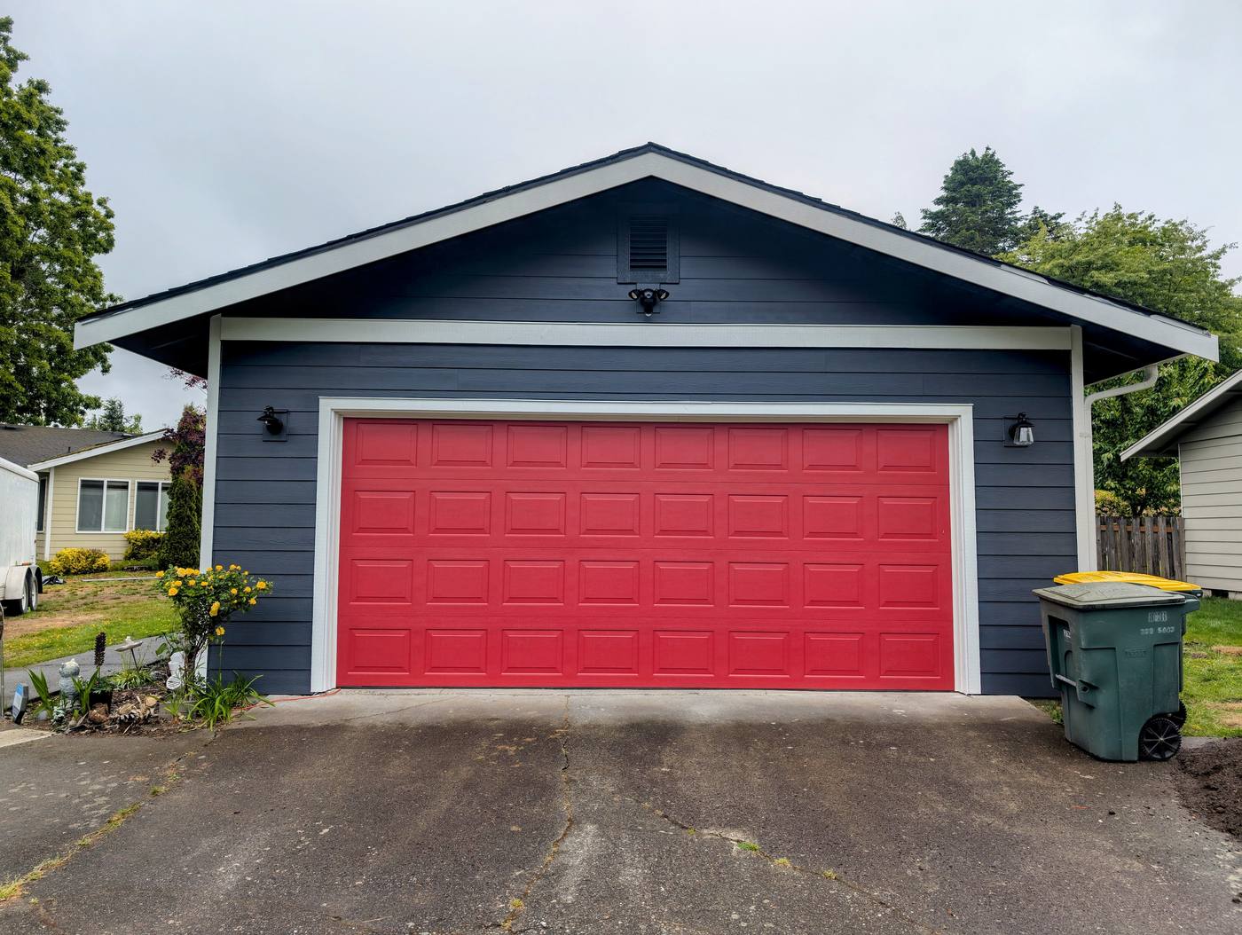 Detached garage in Lynden, Washington with new navy lap siding, white trim, exterior lighting and a red garage door by Premier Construction Services